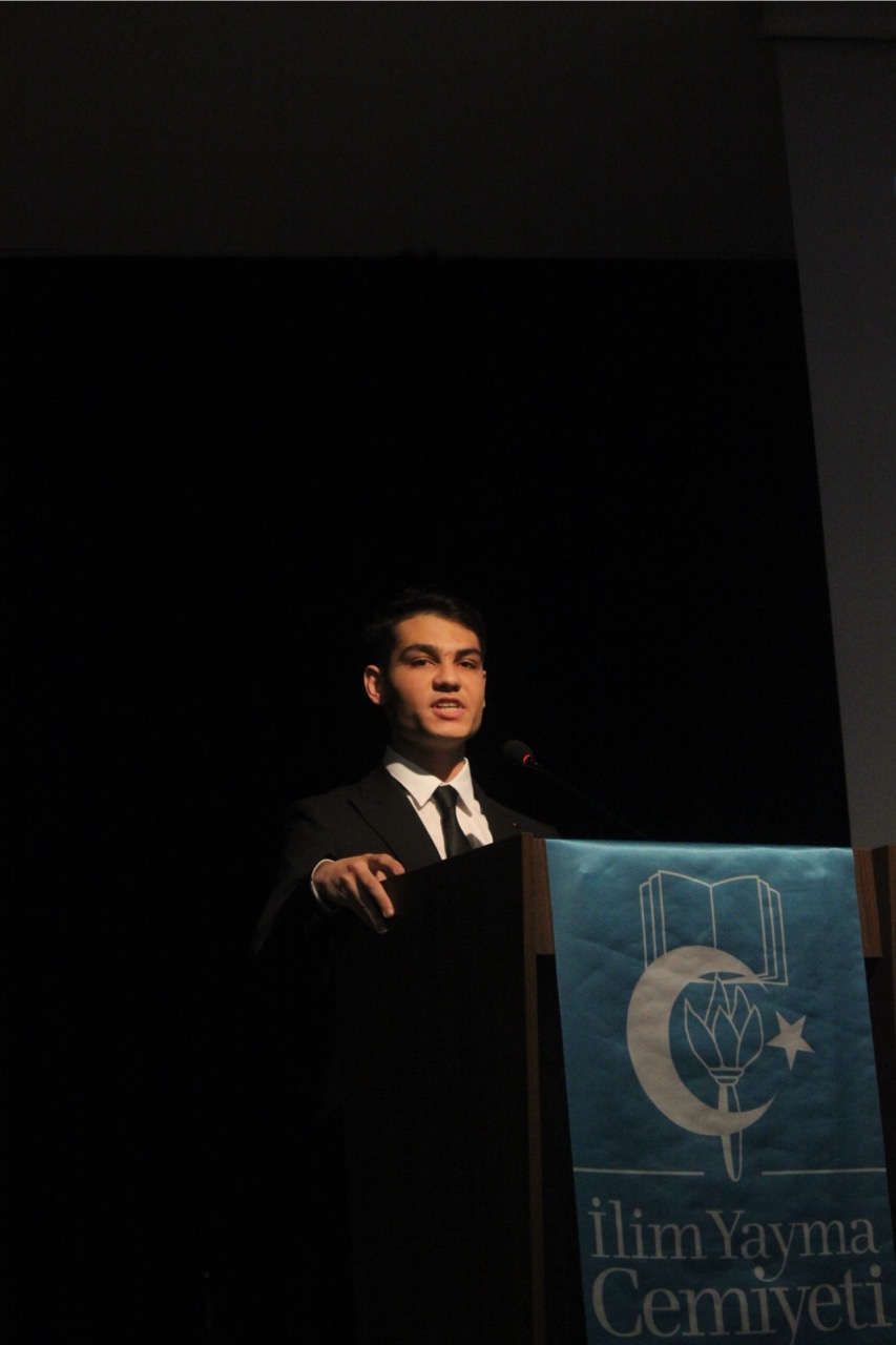 Berkay Mazman giving a speech on the podium of the conference.